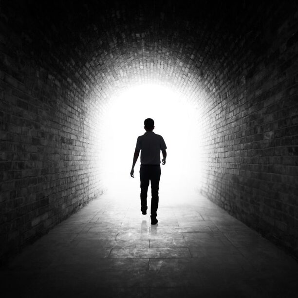 Young man walking through a dark tunnel.